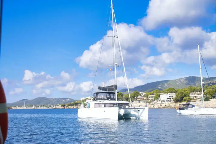 white sailboat on sea near green mountain under blue sky during daytime